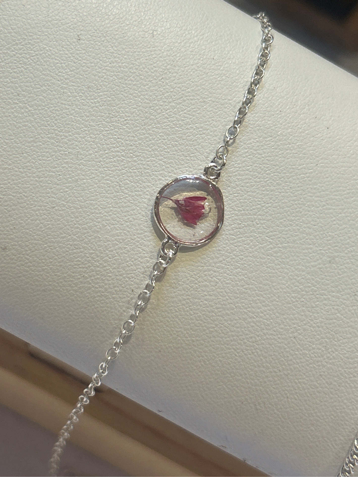 Silver bracelet with a circular charm featuring a pressed flower on a white surface.
