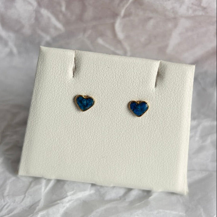 Heart-shaped blue earrings on a white card against a crumpled white background
