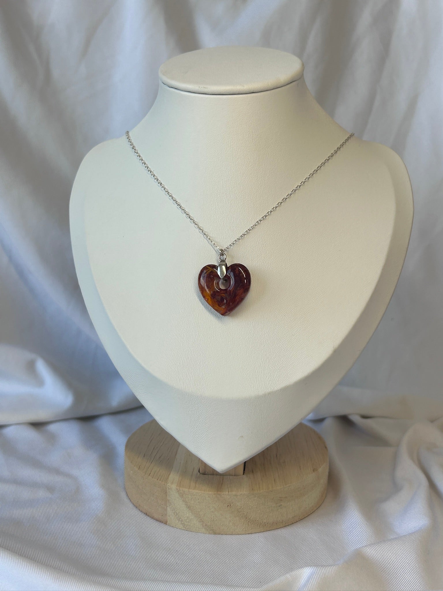 Necklace with a heart-shaped amber coloured flowers pendant on a mannequin bust against a white background