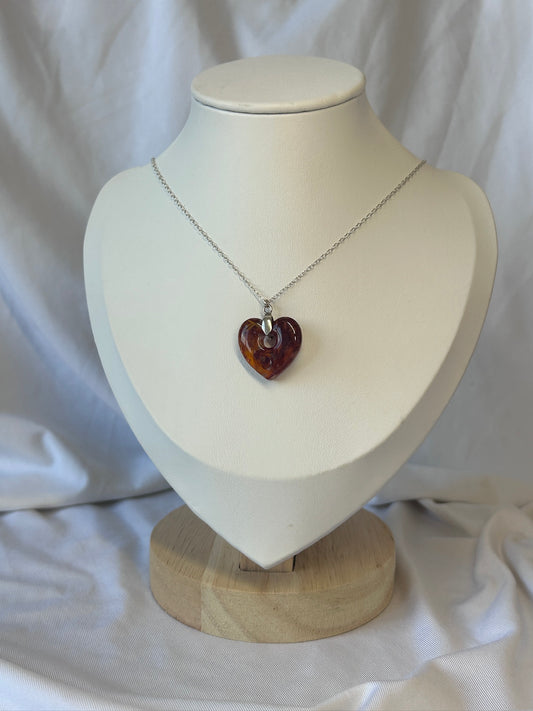 Necklace with a heart-shaped amber coloured flowers pendant on a mannequin bust against a white background