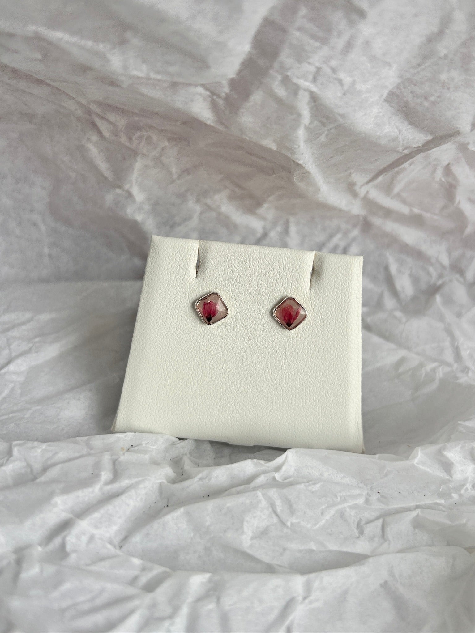 Pair of earrings on a white card with a crumpled white paper background