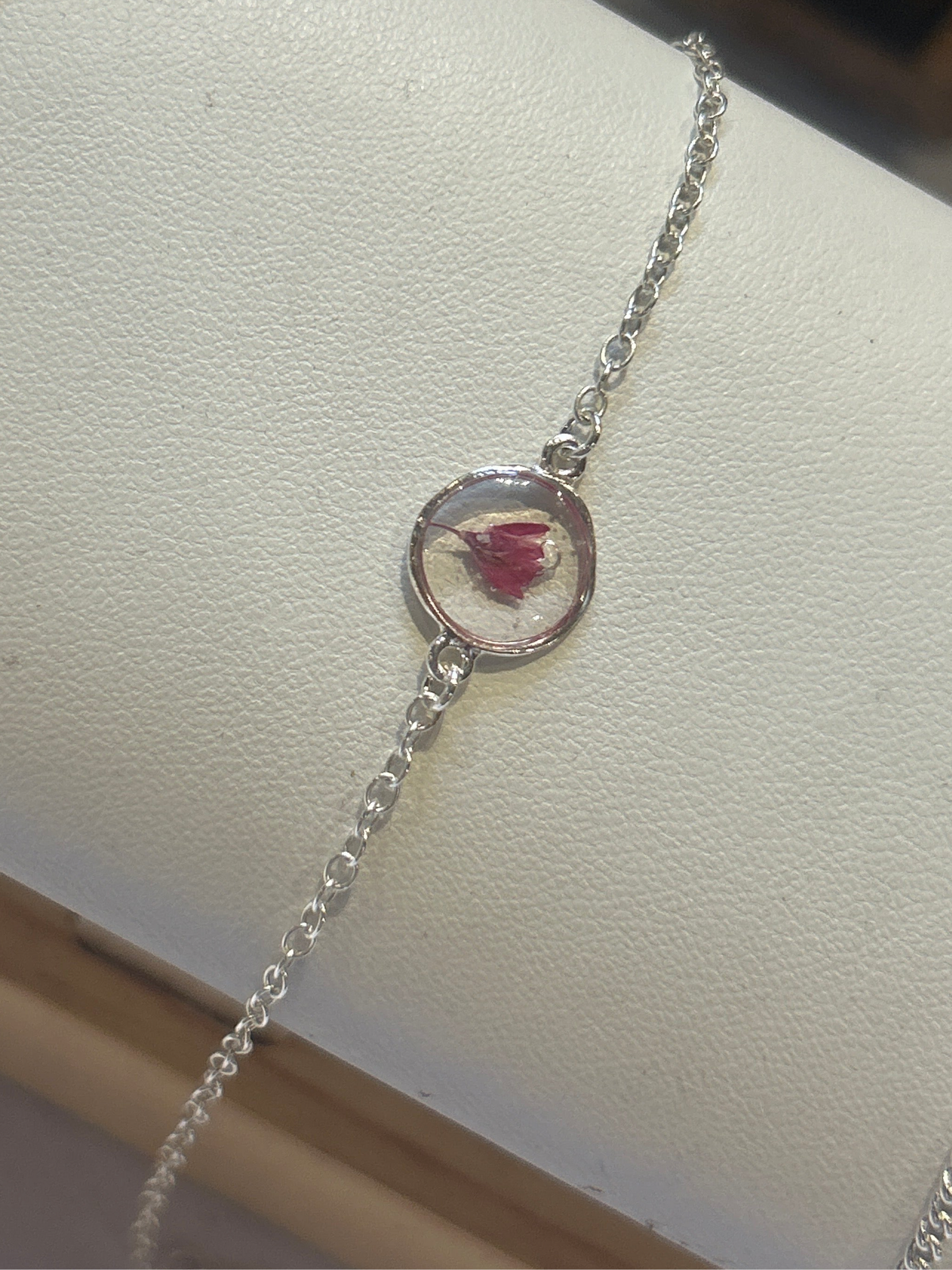 Silver bracelet with a circular charm featuring a pressed flower on a white surface.