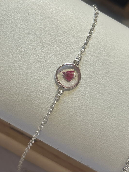 Silver bracelet with a circular charm featuring a pressed flower on a white surface.
