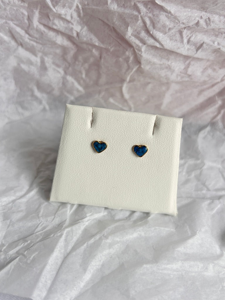 Heart-shaped blue earrings on a white card against a crumpled white background