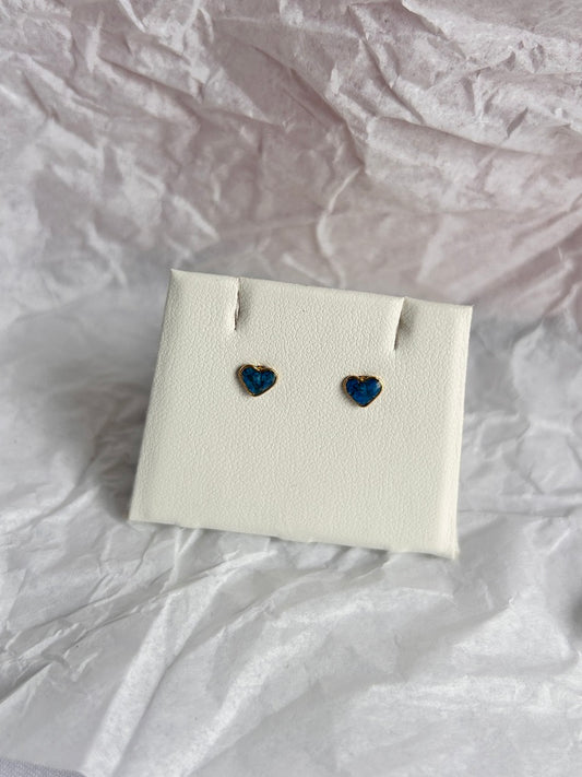 Heart-shaped blue earrings on a white card against a crumpled white background