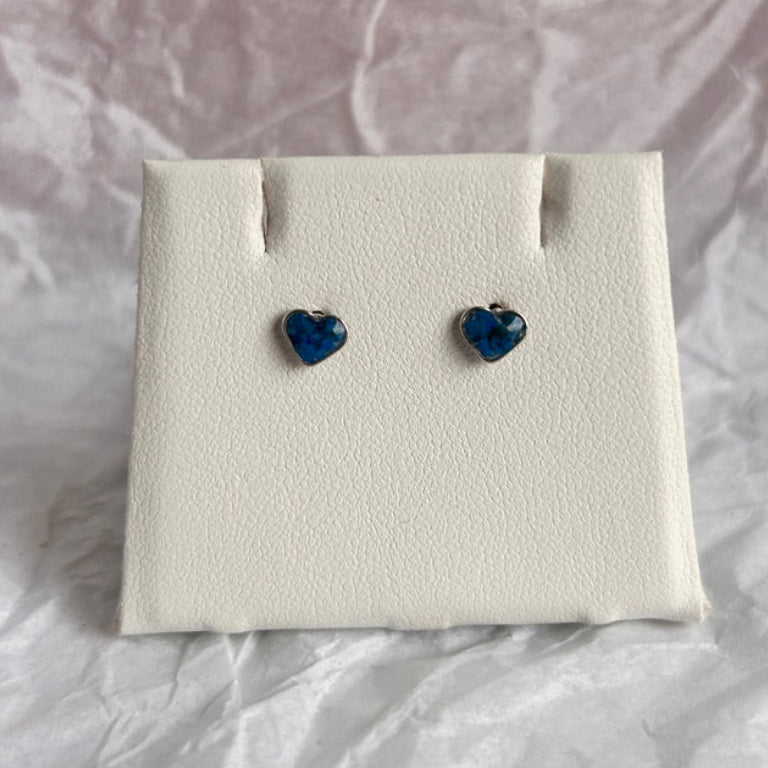 Heart-shaped blue earrings on a white earring display card with a crumpled white paper background.