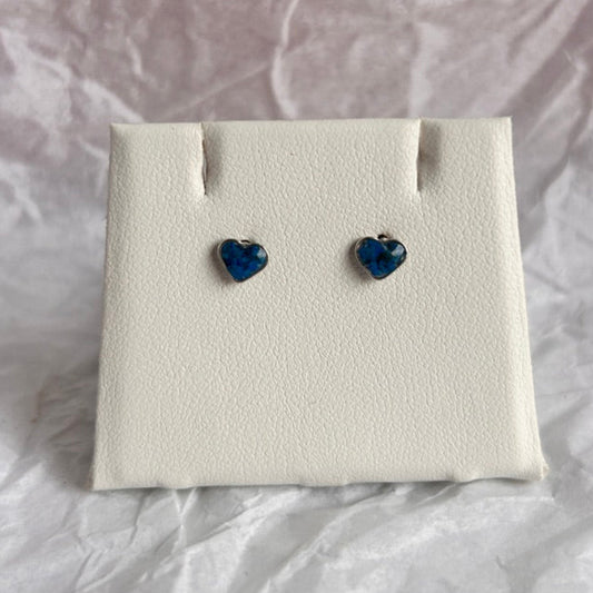 Heart-shaped blue earrings on a white earring display card with a crumpled white paper background.