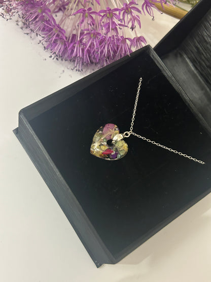 Heart-shaped pendant necklace in a black jewelry box with purple flowers in the background