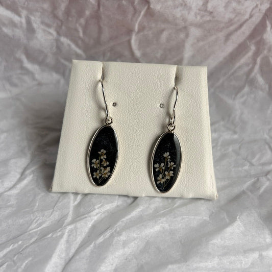Black earrings with floral details on a white card against a textured gray background